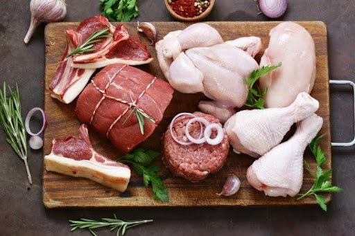 Raw beef and chicken cuts on a wooden board with herbs and spices, illustrating the question “Is organic meat better?”