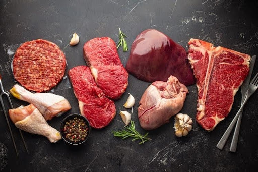 What is organic meat? Selection of raw organic cuts including beef, chicken, and offal displayed on a dark surface.