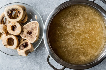 How to Make Bone Broth at Home; agolden homemade bone broth simmering in a large pot for more flavor and rich depth.