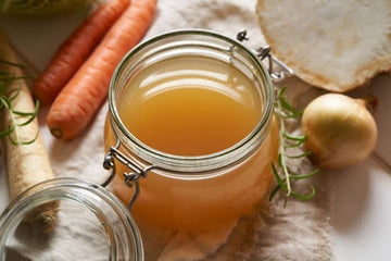 Homemade bone broth in a glass jar with fresh vegetables.