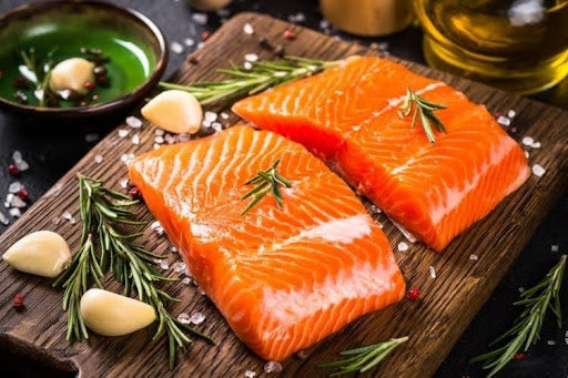 How to cook salmon: fresh organic salmon fillets seasoned with rosemary, garlic, and sea salt on a wooden board.